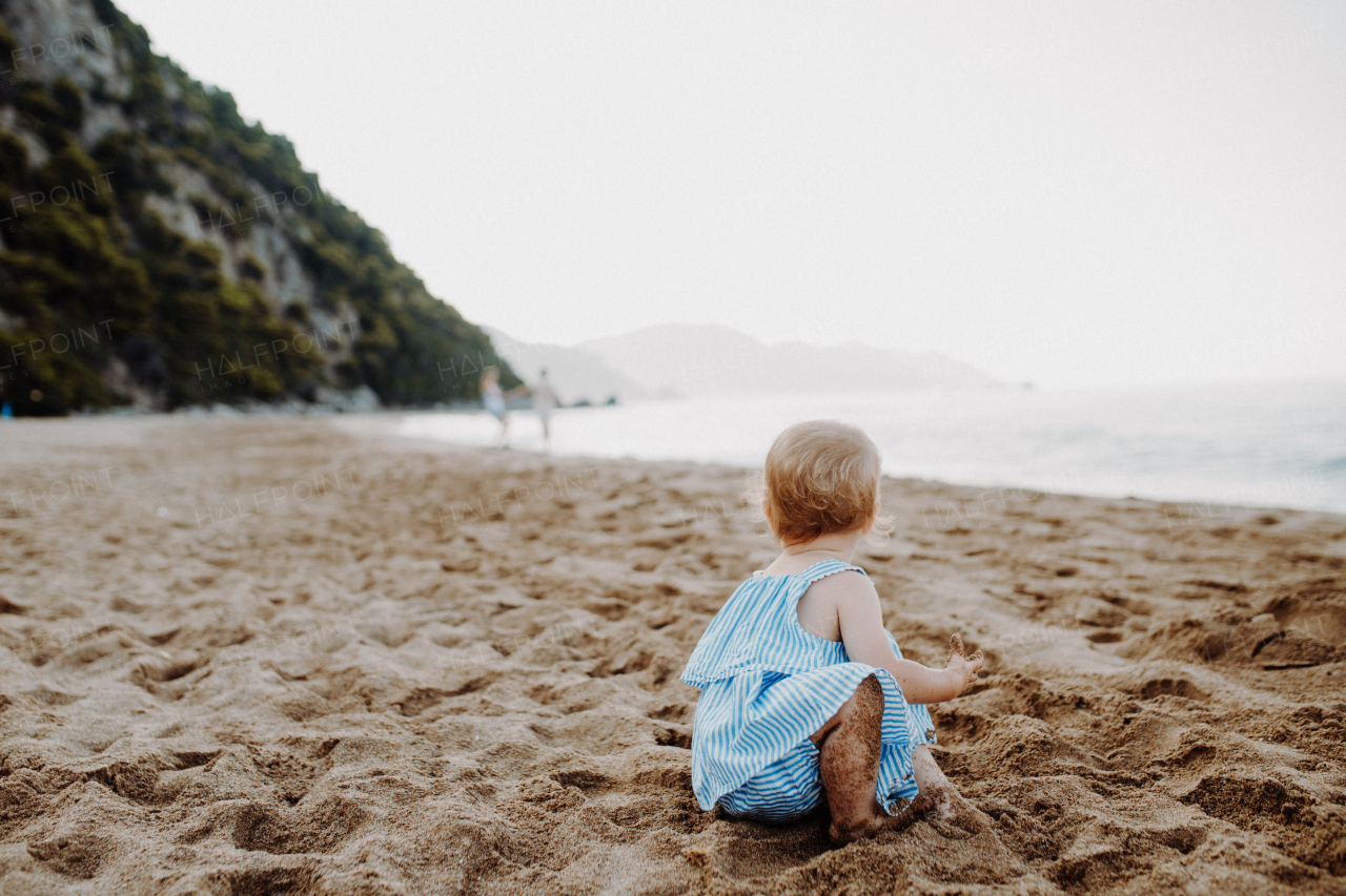 A small toddler girl playing in sand on beach on summer holiday. Copy space.