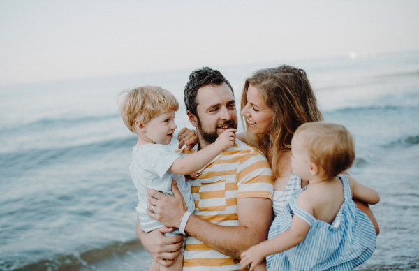 A family with two toddler children walking on beach on summer holiday. A father and mother carrying son and daughter in the arms.