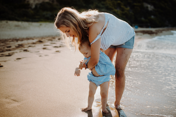 A young mother with small toddler daughter walking on beach on summer holiday.