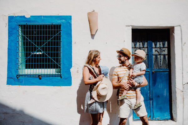 A young family with two toddler children and hats walking in town on summer holiday.