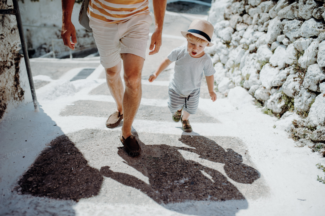 A midsection of unrecoognizable father with toddler son walking in town on summer holiday.