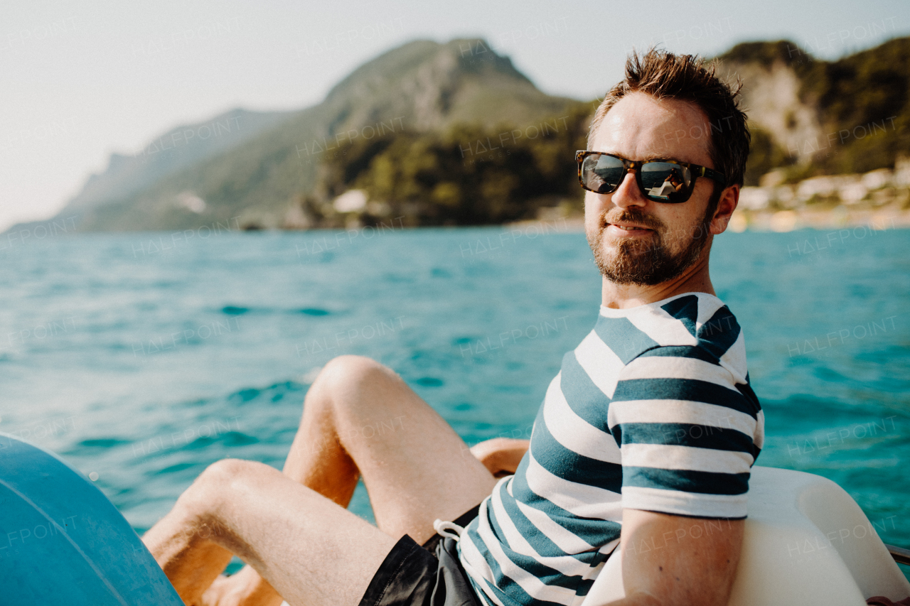 Mature man with sunglasses sitting on boat on summer holiday, looking at camera.