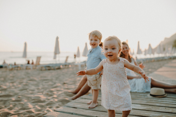 A young family with toddler children having fun on beach on summer holiday.