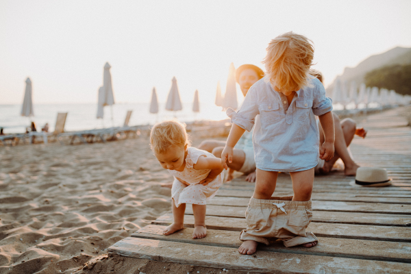 A young family with toddler children having fun on beach on summer holiday.