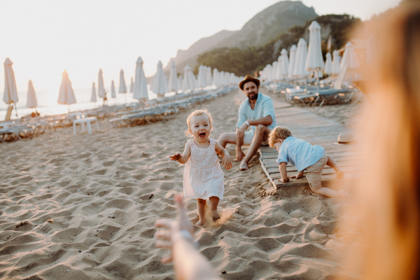 A young family with toddler children having fun on beach on summer holiday.