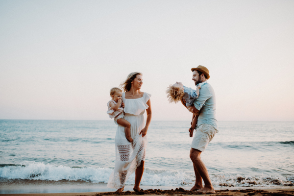 A young family with two toddler children standing on beach on summer holiday, laughing.