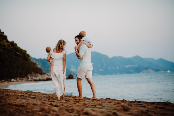 A rear view of young family with two toddler children walking on beach on summer holiday.