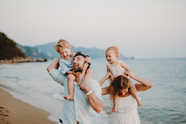 A happy young family with two toddler children walking on beach on summer holiday.