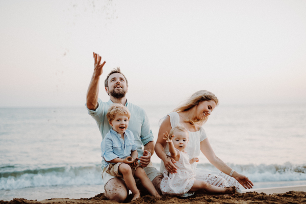 A family with two toddler children sitting on sand beach on summer holiday, playing.