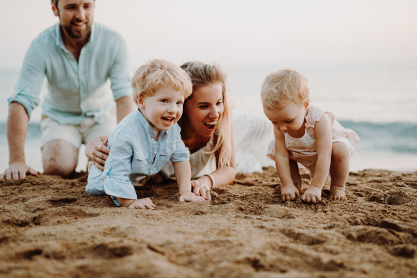 A family with two toddler children lying on sand beach on summer holiday, playing.