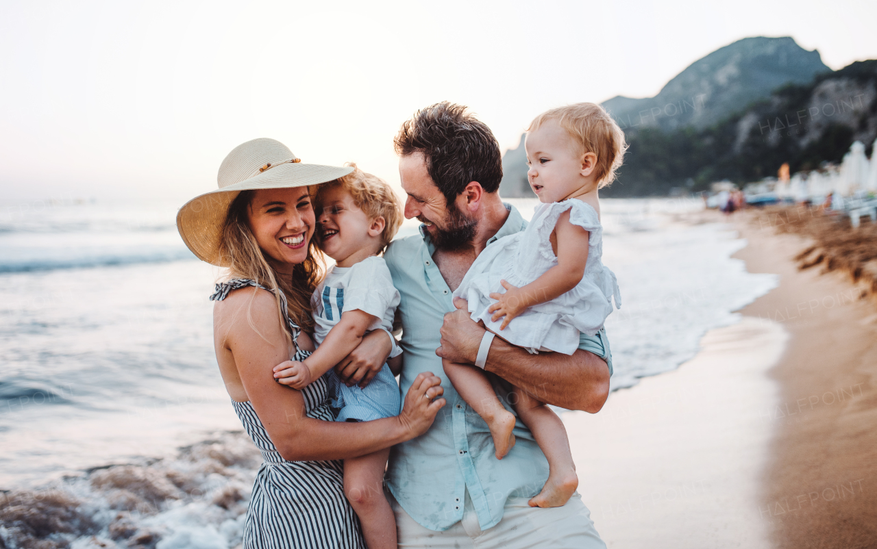 A young family with two toddler children standing on beach on summer holiday, laughing.