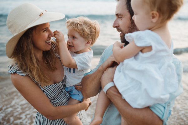 A young family with two toddler children standing on beach on summer holiday, laughing.