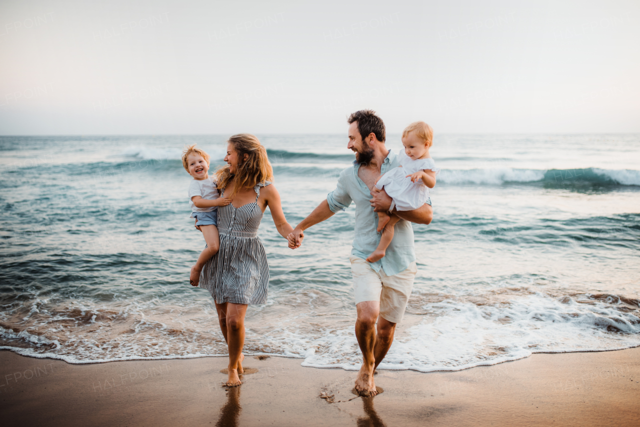 A young family with two toddler children walking on beach on summer holiday.