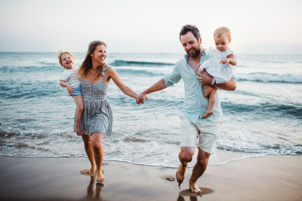 A young family with two toddler children walking on beach on summer holiday, holding hands.