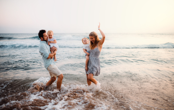 A young family with two toddler children standing on beach on summer holiday, having fun.