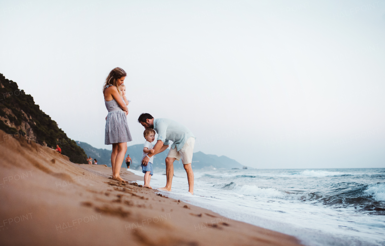 A young family with two toddler children standing on beach on summer holiday, having fun.