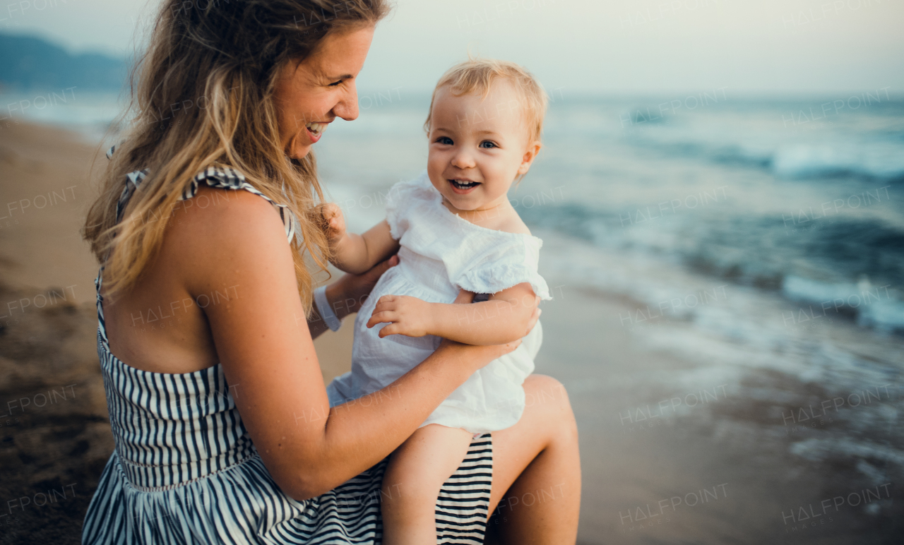 A young mother with a toddler girl sitting on beach on summer holiday.