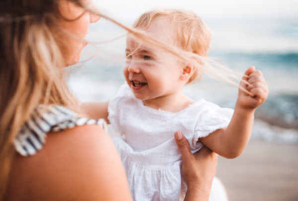 A close-up of young mother with a toddler girl on beach on summer holiday.