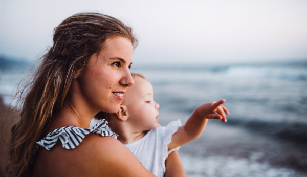 A close-up of young mother with a toddler girl on beach on summer holiday.