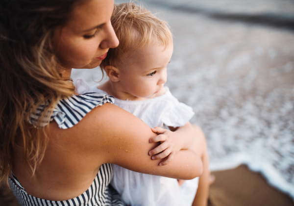 A close-up of young mother with a toddler girl on beach on summer holiday.