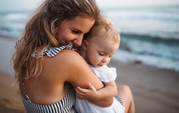 A close-up of young mother with a toddler girl on beach on summer holiday.