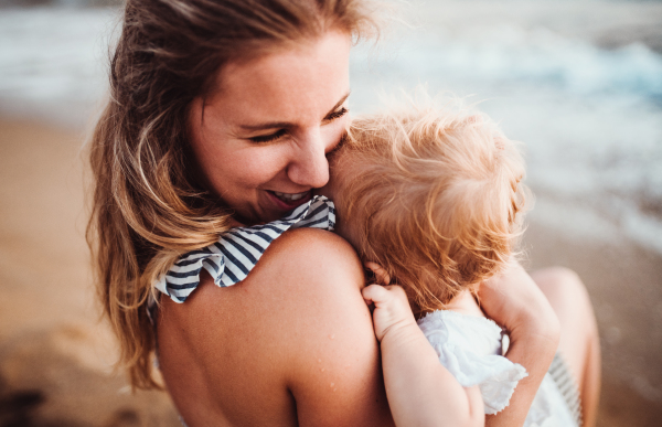 A close-up of young mother with a toddler girl on beach on summer holiday.