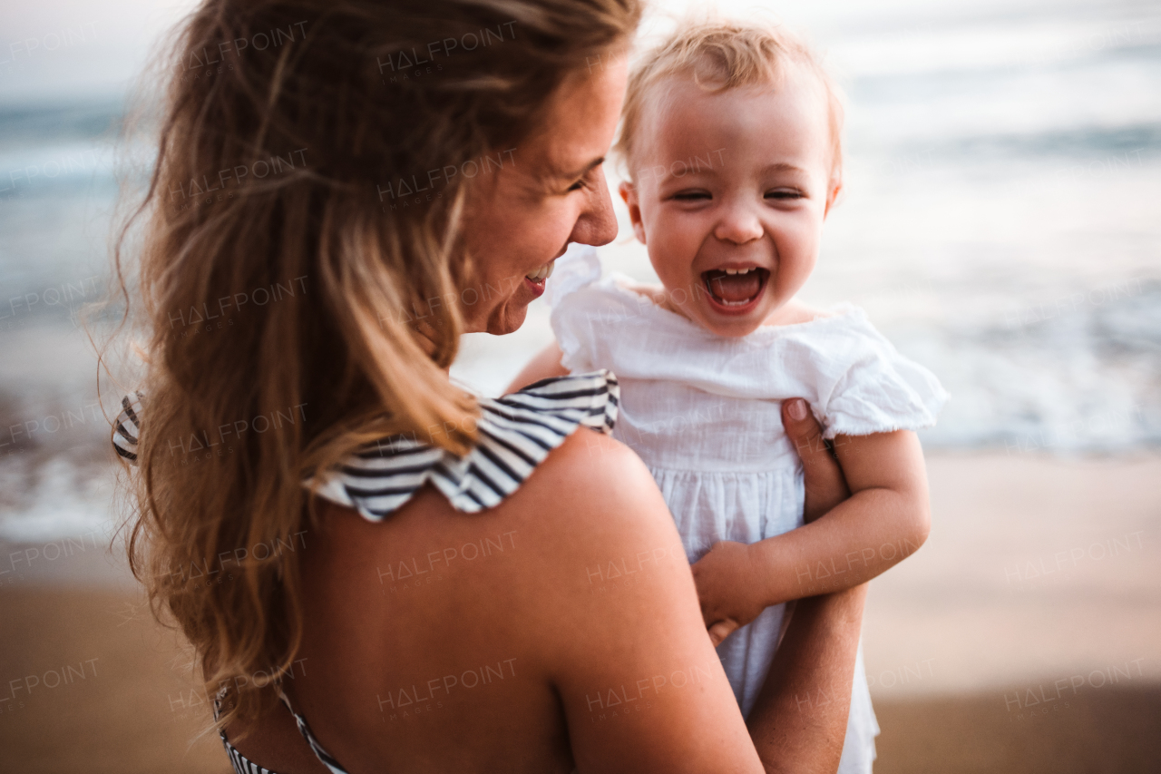 A close-up of young mother with a toddler girl on beach on summer holiday.