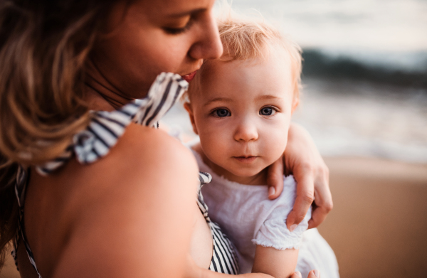 A close-up of young mother with a toddler girl on beach on summer holiday.