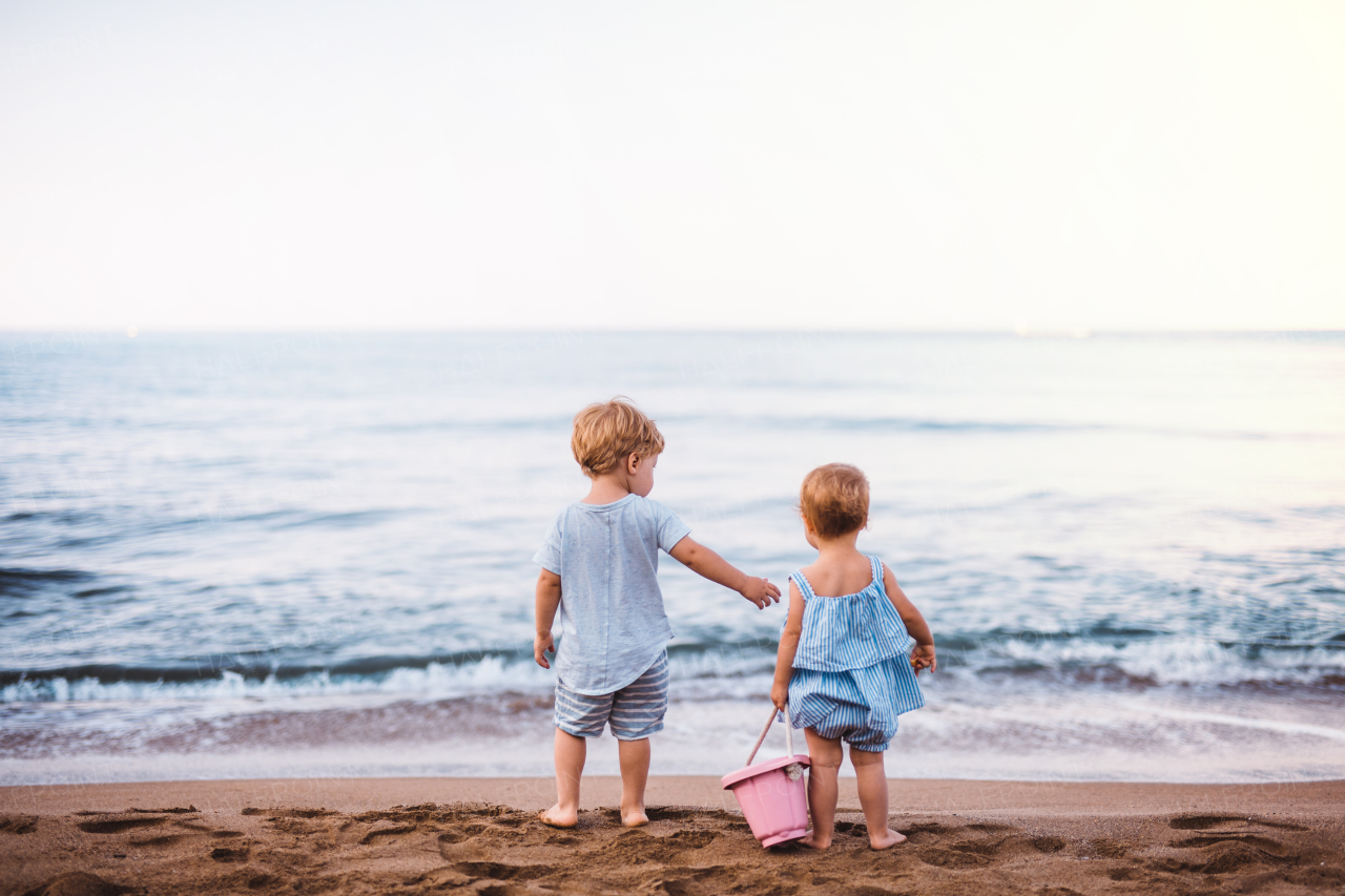 A rear view of two toddler children playing on sand beach on summer family holiday.