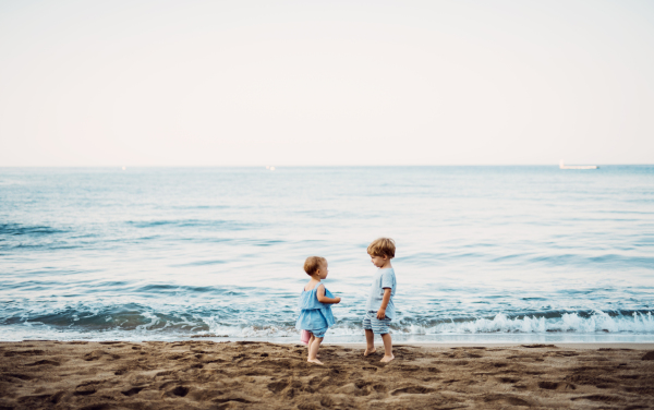 Two toddler children playing on sand beach on summer family holiday.