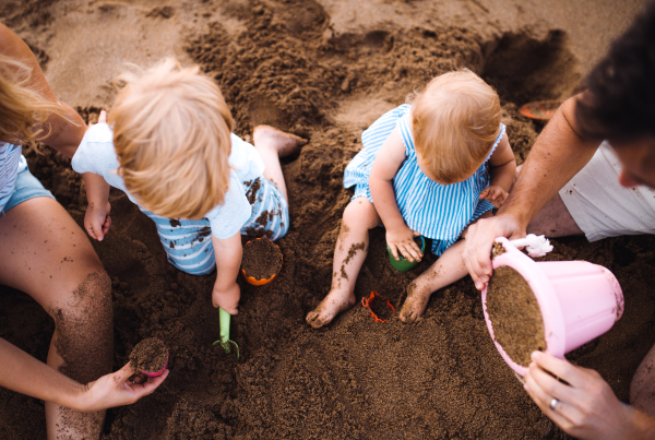 A young family with toddler children playing with sand on beach on summer holiday, a top view and midsection.