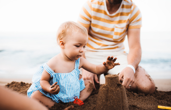 Midsection of father with a toddler girl playing on beach on summer holiday.