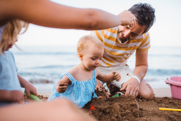 A young family with toddler children playing on sand beach on summer holiday.