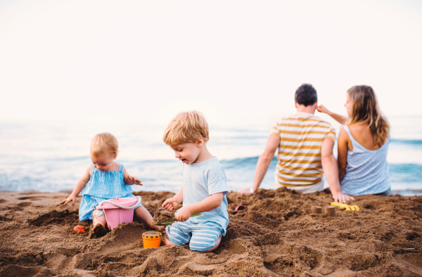 Toddler children with parents playing on sand beach on summer family holiday.