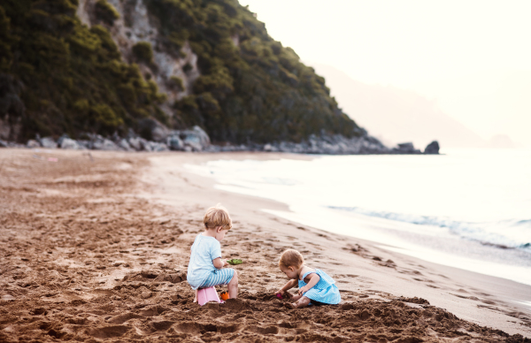 Two toddler children playing on sand beach on summer family holiday.