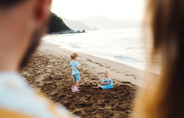 Parents and toddler children playing on sand beach on summer family holiday.