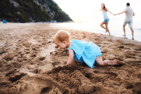 A small toddler girl playing in sand on beach on summer holiday. Copy space.