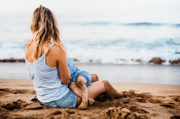 A young mother breasfeeding toddler daughter on beach on summer holiday.