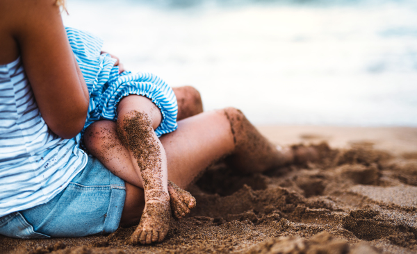 A midsection of unrecognizable young mother breasfeeding toddler daughter on beach on summer holiday.