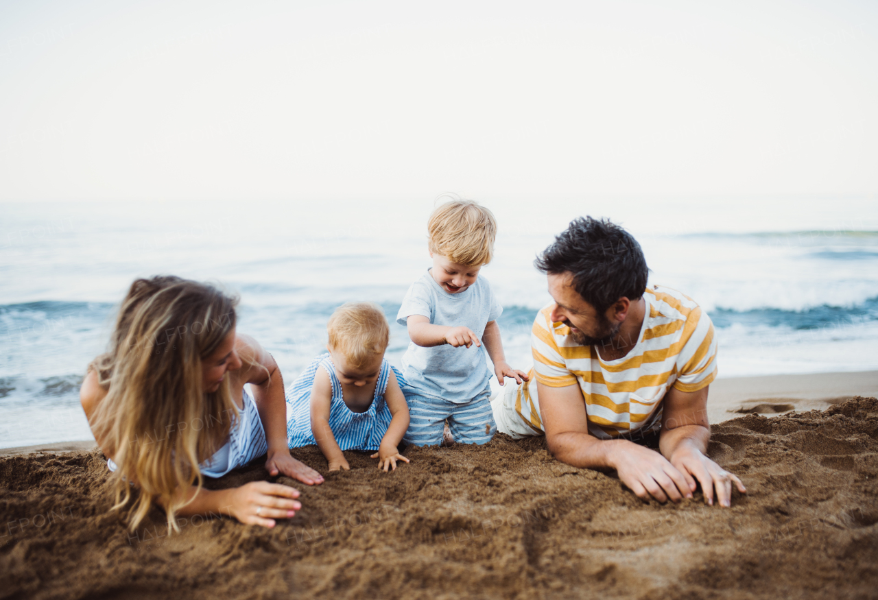 A family with two toddler children lying on sand beach on summer holiday, playing.