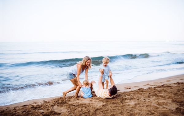 A family with two toddler children lying on sand beach on summer holiday, playing.