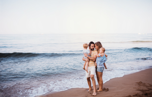 A young family with two toddler children standing on beach on summer holiday. Copy space.