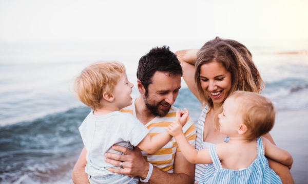 A young family with two toddler children walking on beach on summer holiday.