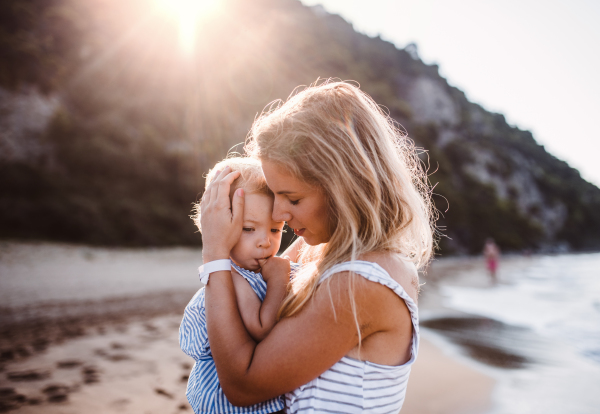 Young mother hugging a toddler girl on beach on summer holiday at sunset.