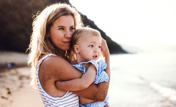 A happy young mother with a toddler girl on beach on summer holiday.