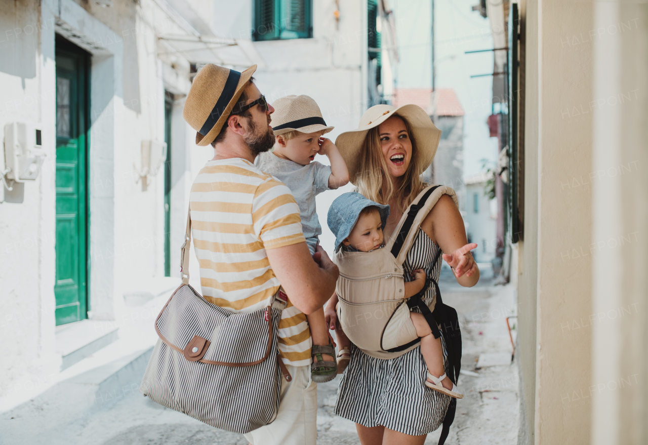 A young family with two toddler children and hats walking in town on summer holiday.