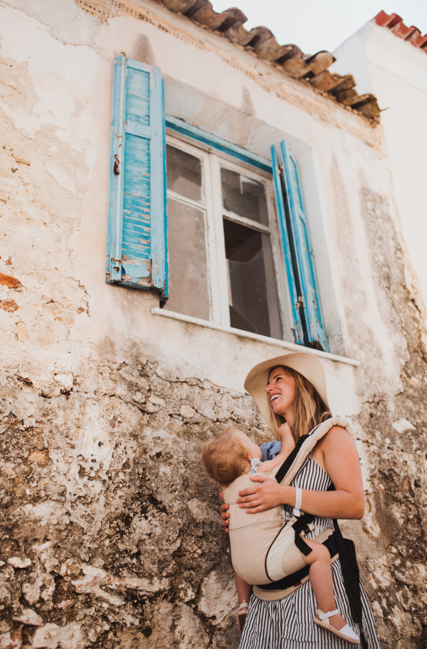 A young mother with a baby in a carrier walking in town on summer holiday. Copy space.