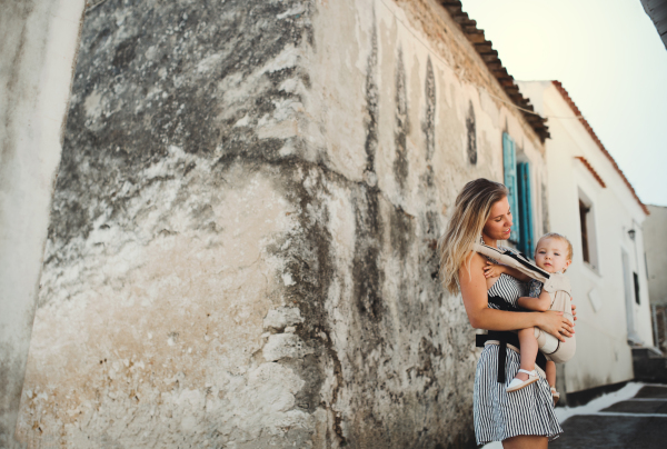 A young mother with a baby in a carrier walking in town on summer holiday. Copy space.