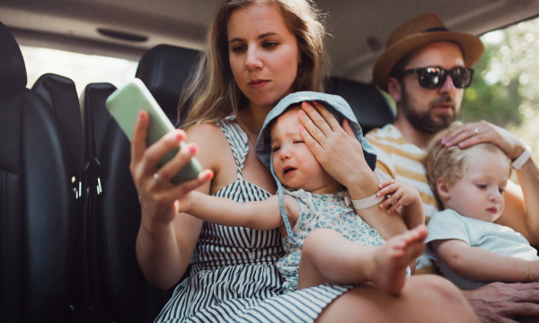 A young family with two toddler children in taxi car on summer holiday, using smartphone.