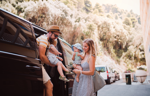 A young family with two toddler children getting out of taxi car on summer holiday.